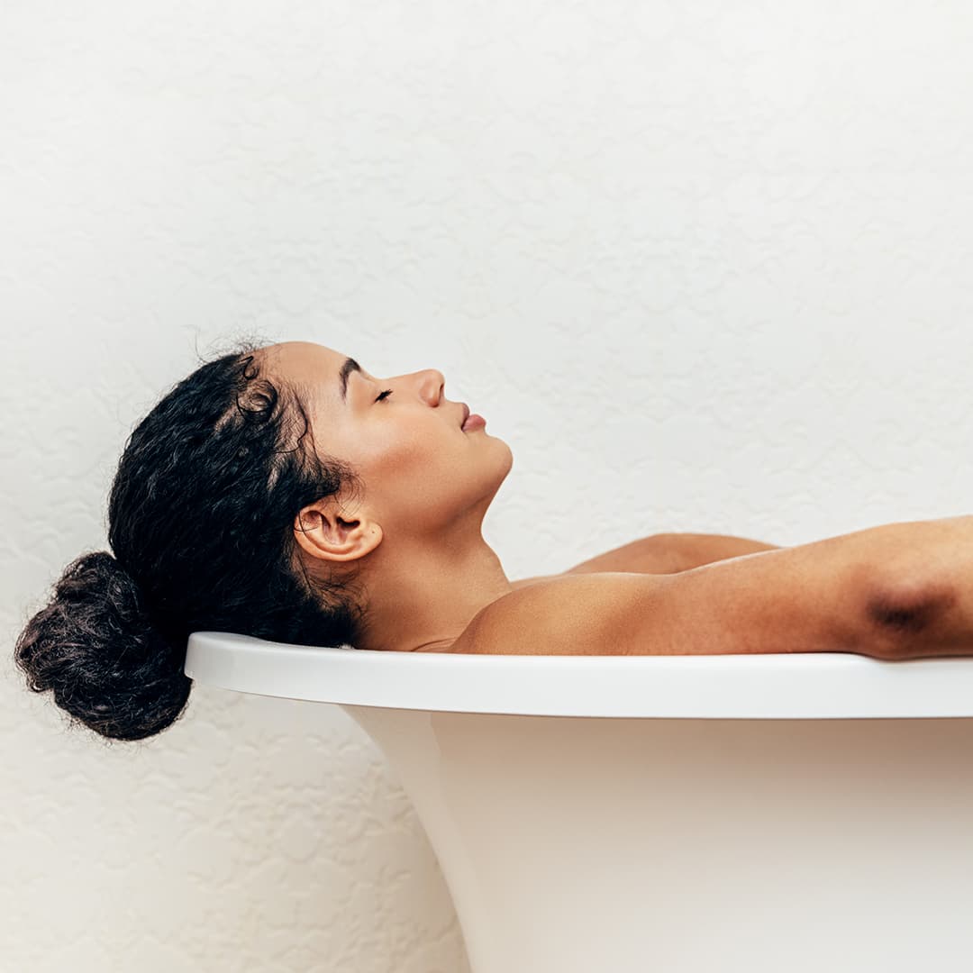 A photo of a woman with a bun hairstyle relaxing on a bathtub