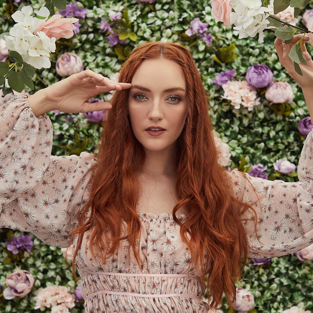 Image of a model with wavy hair and floral outfit posing in the garden