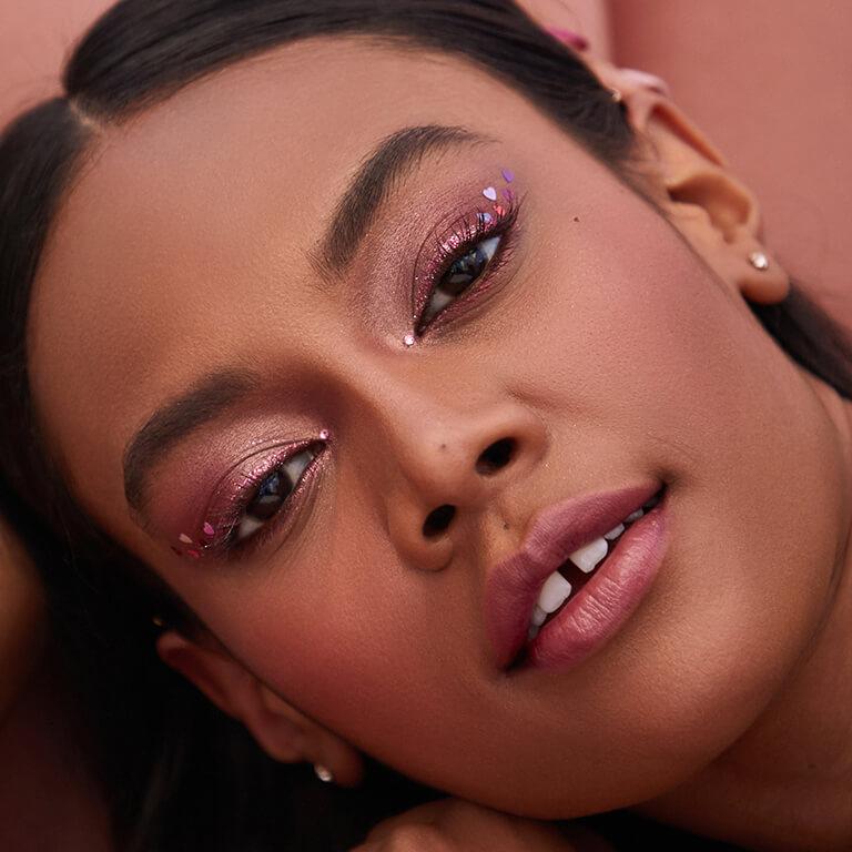 A closeup image of a model wearing rose gold eyeshadow with glitter heart sequins