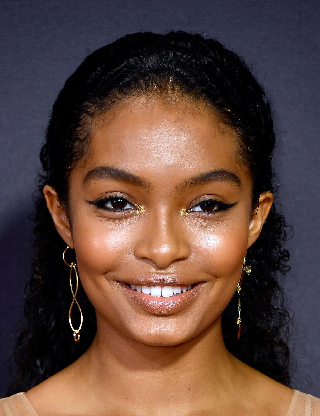Close-up look of Yara Shahidi rocking a simple yet bold look featuring cat eyeliner, with a touch of gold lip gloss wearing a gold dangling earring