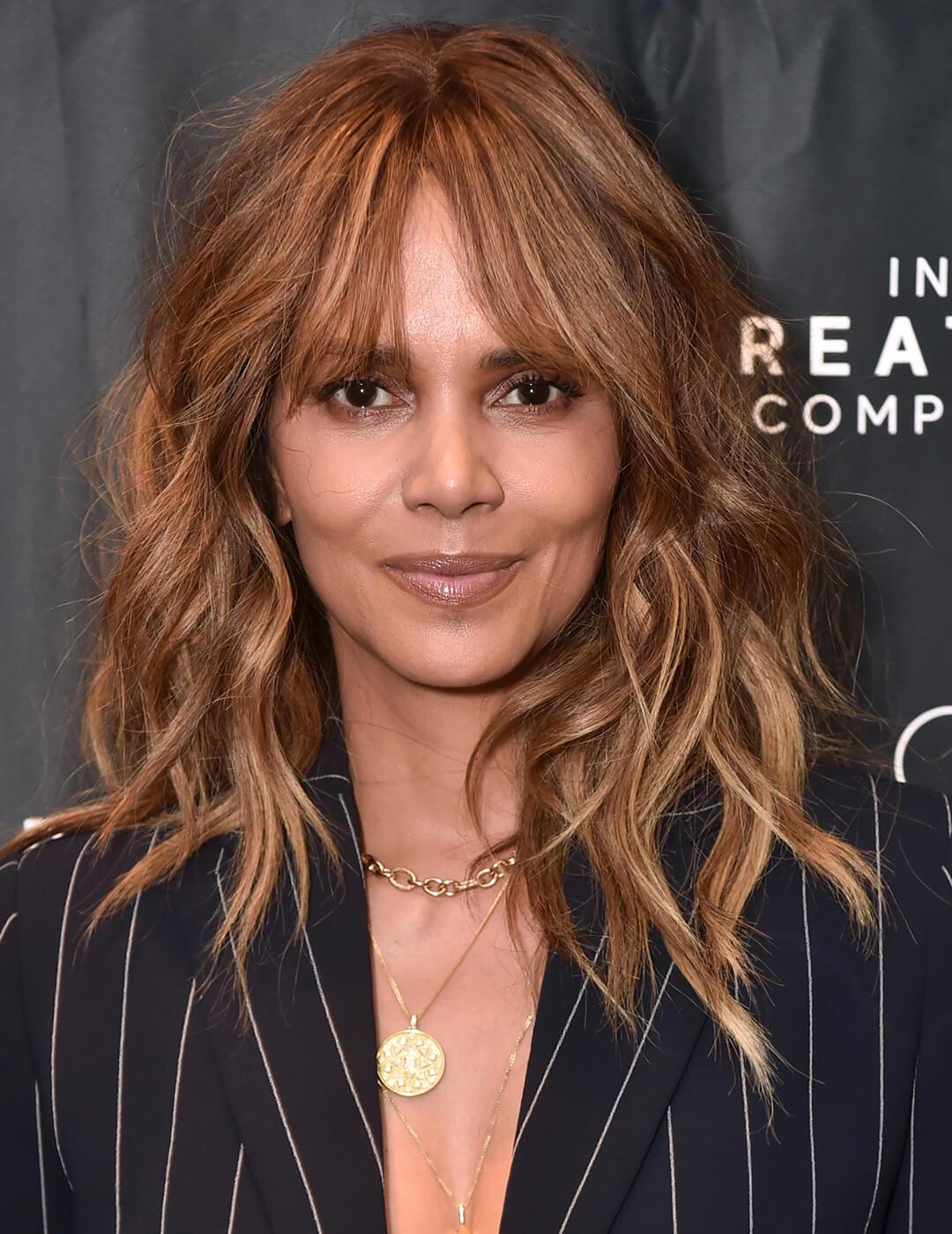 A photo of Halle Berry with a front feathering hairstyle with brown highlights wearing a black coat