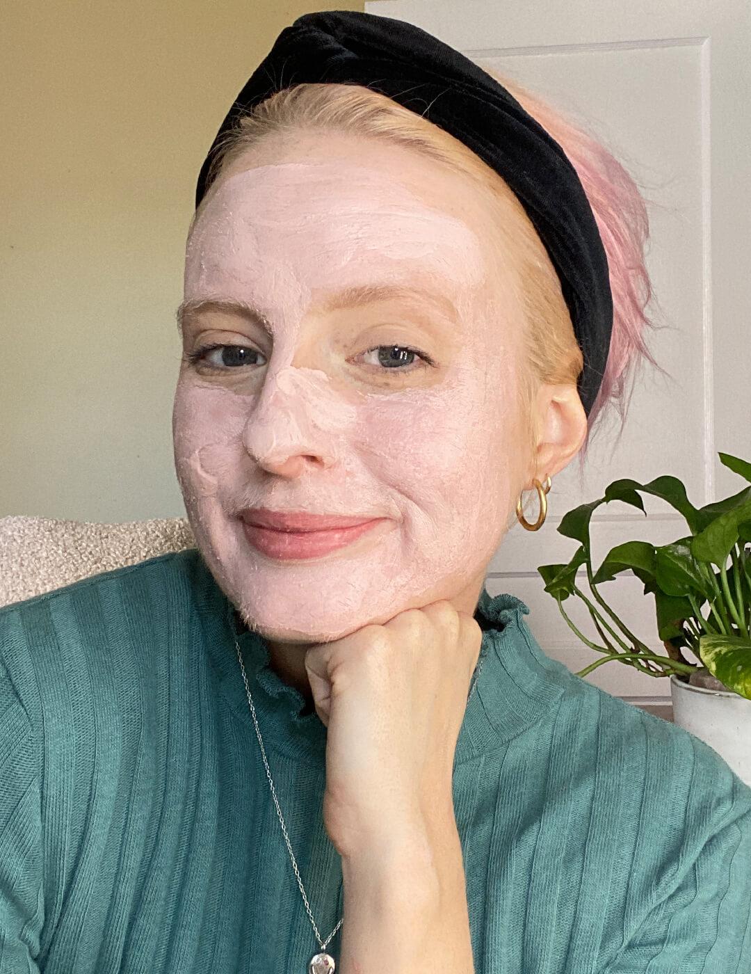 Hannah Cassidy in a green sweater and black headband posing with pink mud mask on her face