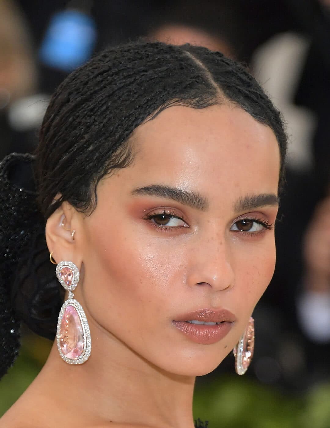 Close-up look of  Zoe Kravitz flaunting a minimal makeup look while rocking her chic micro braids wearing multicolor rhinestone water drop earrings