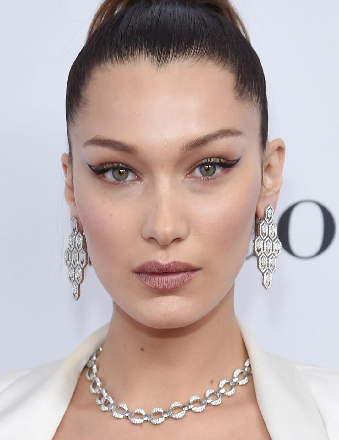 Bella Hadid looking fierce in a white dress, silver necklace and earrings, and a negative space eyeliner makeup look