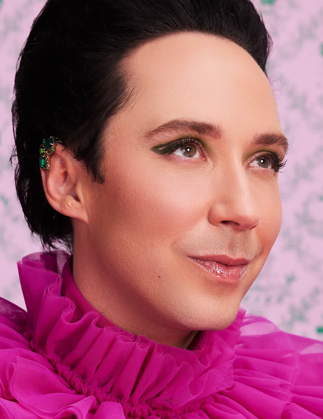 A photo of Johnny Weir wearing a pink fluffy dress with negative-spaced winged eyeliner on a pink background