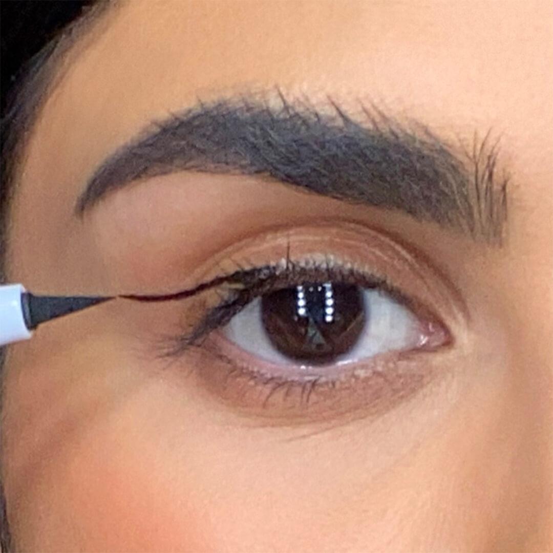 Close-up of a woman drawing a line on her eyelid with an eyeliner
