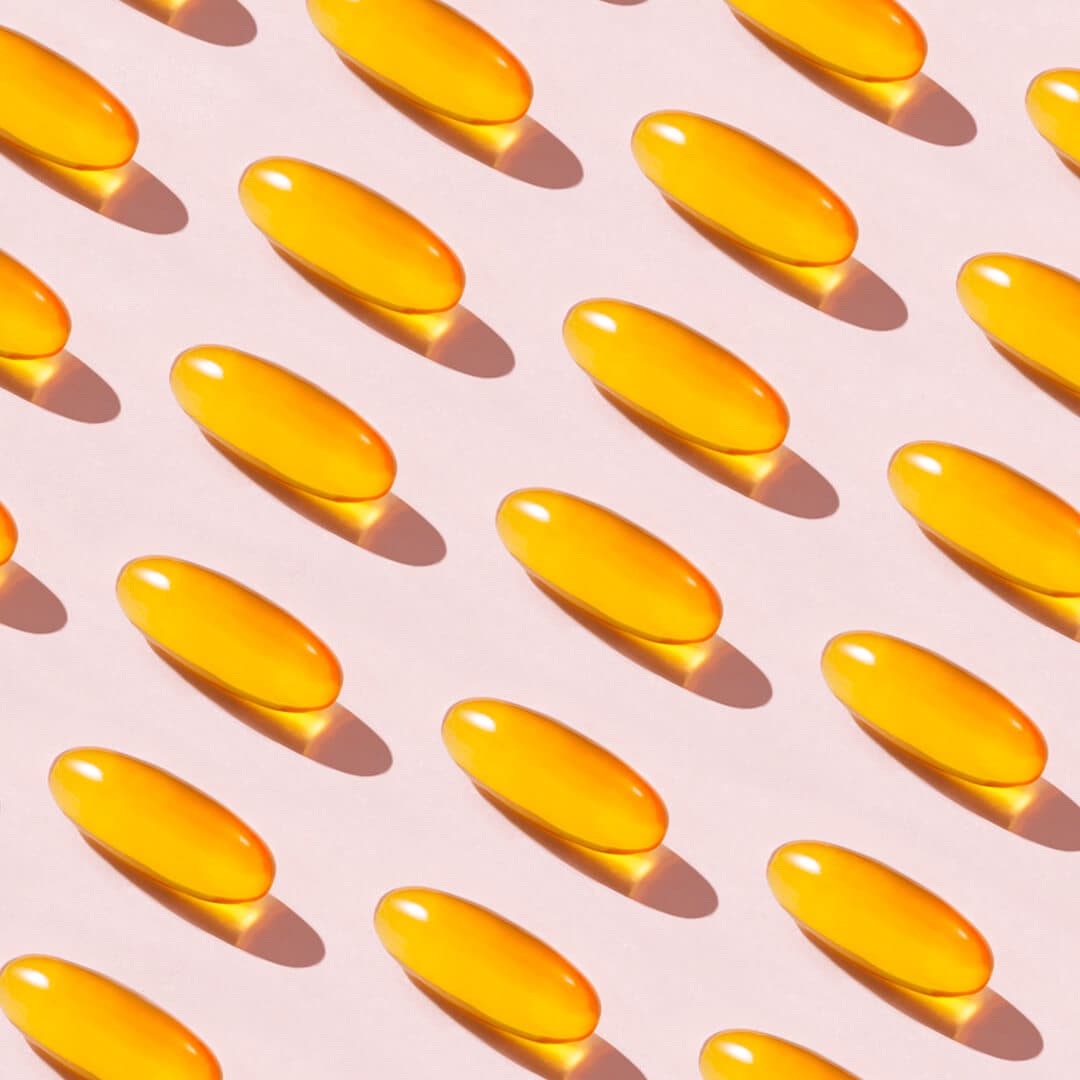 A photo of soft fish oil capsules on a pink background