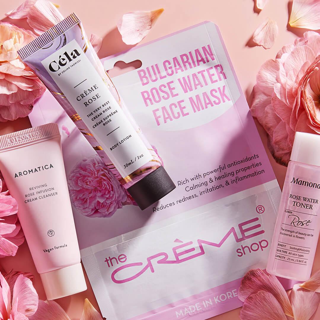 Image of AROMATICA Reviving Rose Infusion Cream Cleanser, CÉLA Crème Rose, THE CRÈME SHOP Bulgarian Rose Water Face Mask, MAMONDE Rose Water Toner, and rose flower and petals on peach background