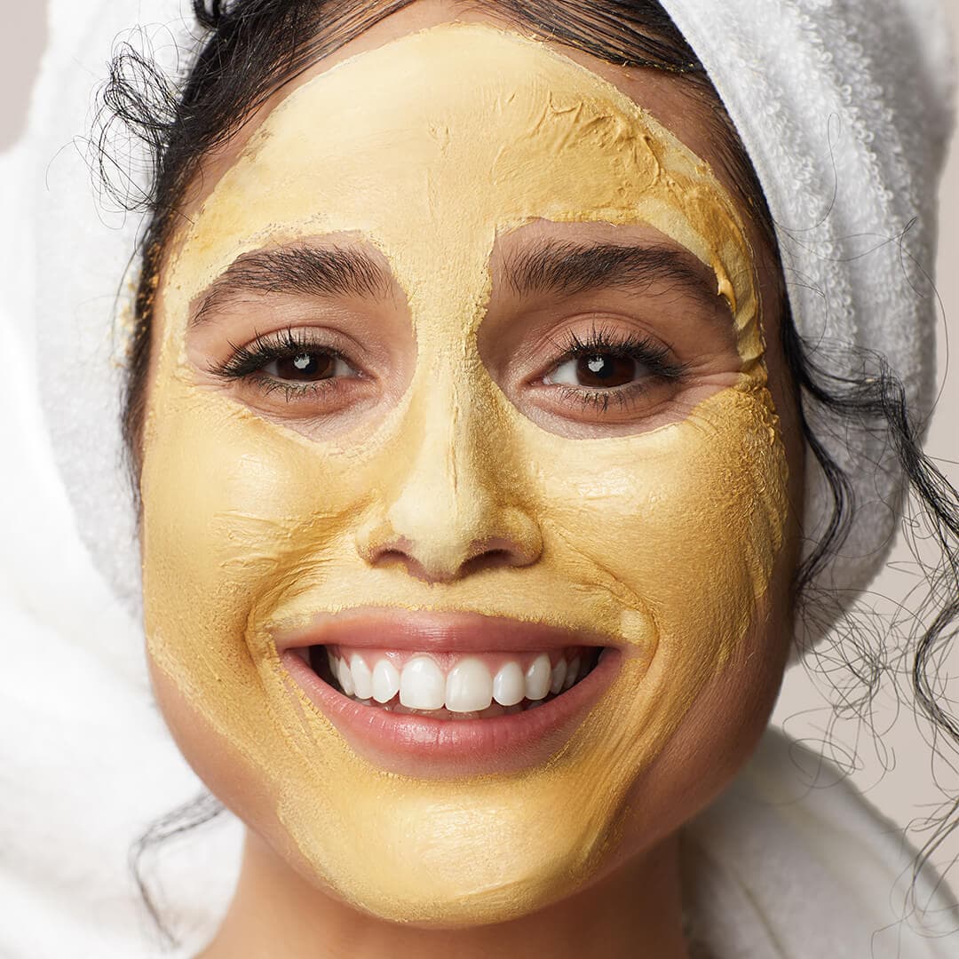 Close-up of a smiling model with gold mud mask on her face