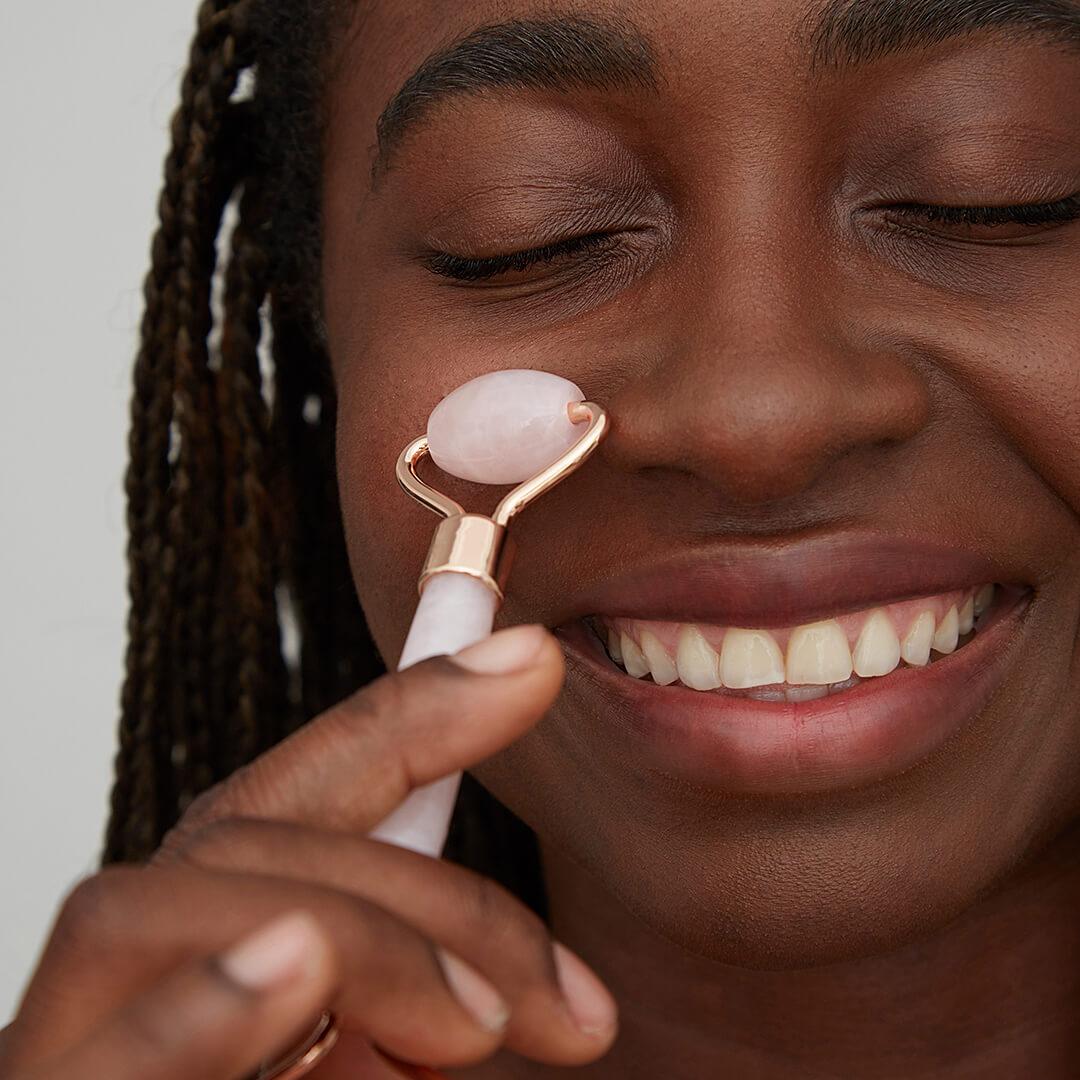 Close-up of a smiling beautiful woman using a rose quartz face roller on her cheek