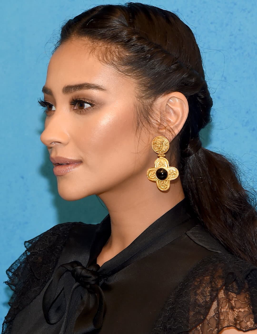 Shay Mitchell rocking a sheer black dress, gold earrings, and twist back ponytail hairstyle