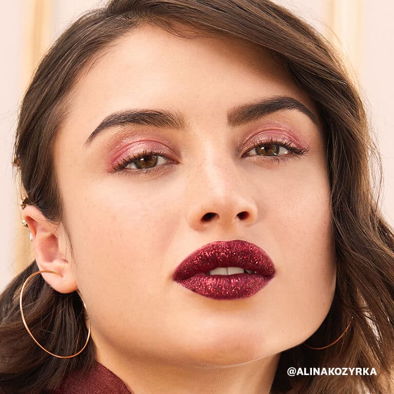 An image of a model wearing glossy rose gold eye shadow and glittery dark berry lipstick