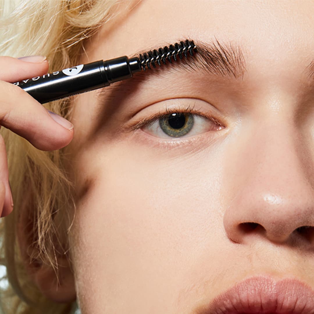 A closeup photo of a model using a spoolie on her eyebrows
