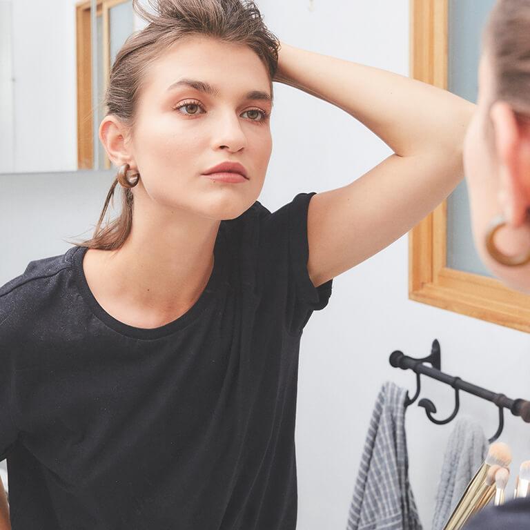 A girl in black shirt looking at herself in the mirror while holding her hair back
