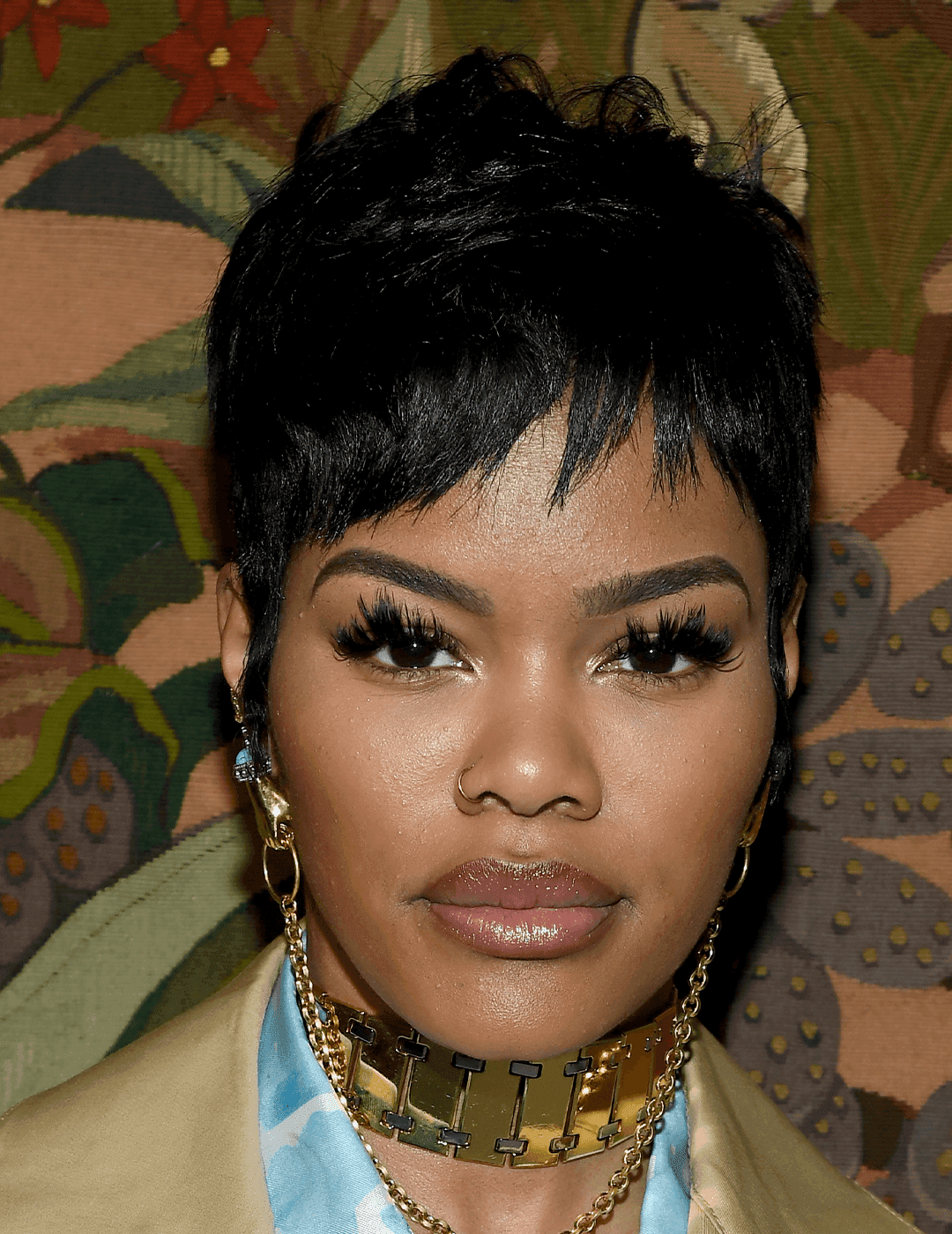 Teyana Taylor rocking a choppy pixie cut hairstyle, dangling gold earrings, gold chain choker, and neutral makeup look