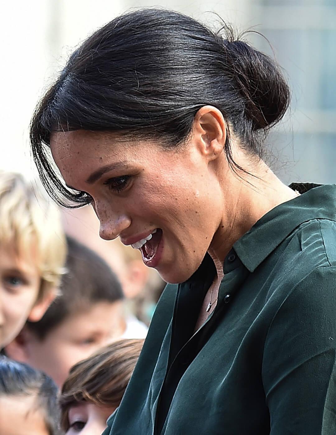 Meghan Markle, Duchess of Sussex, greeting children and sporting a messy chignon hairstyle