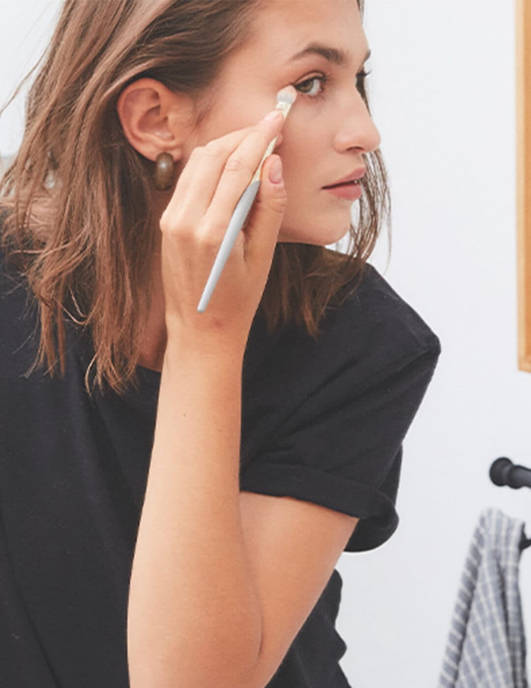 An image of a woman looking at the mirror while applying cosmetics in her eye area