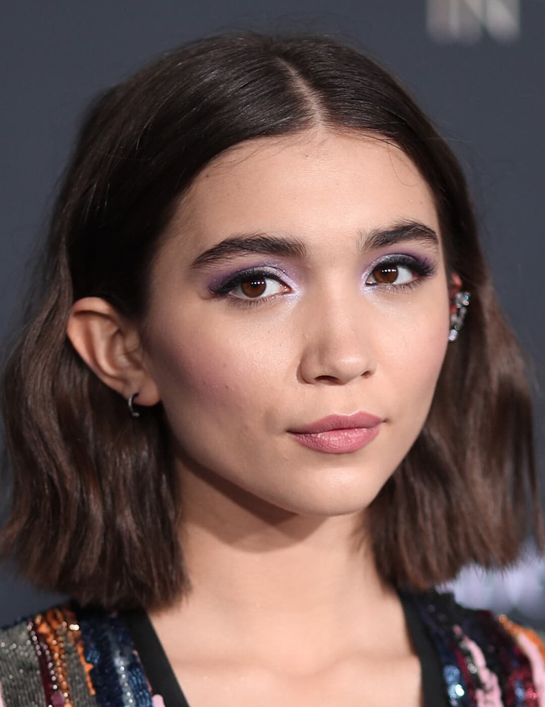 A photo of Rowan Blanchard with her hair tucked in both of her ears revealing her oval-shaped face on a black background
