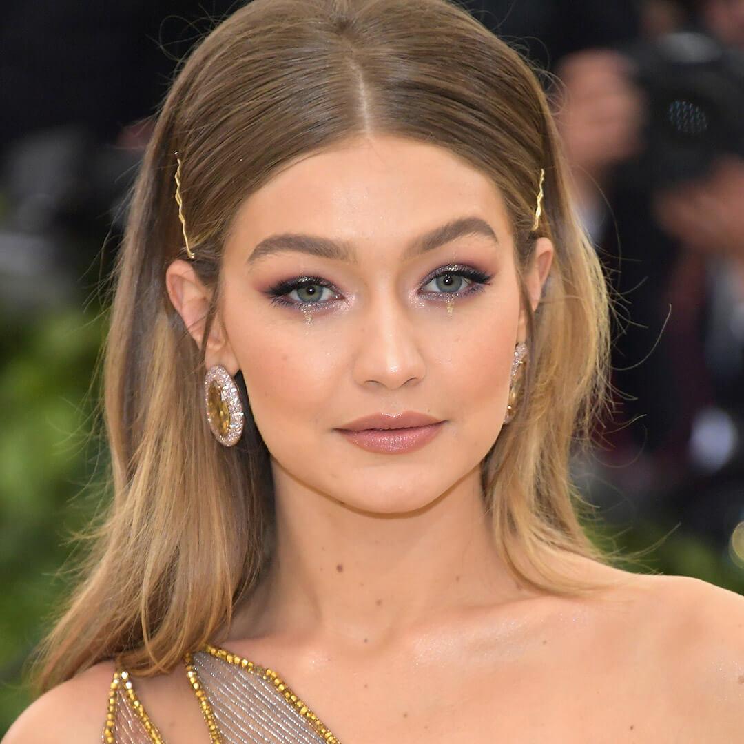Gigi Hadid looking glam in a gold dress and accessories and pinned back hairstyle