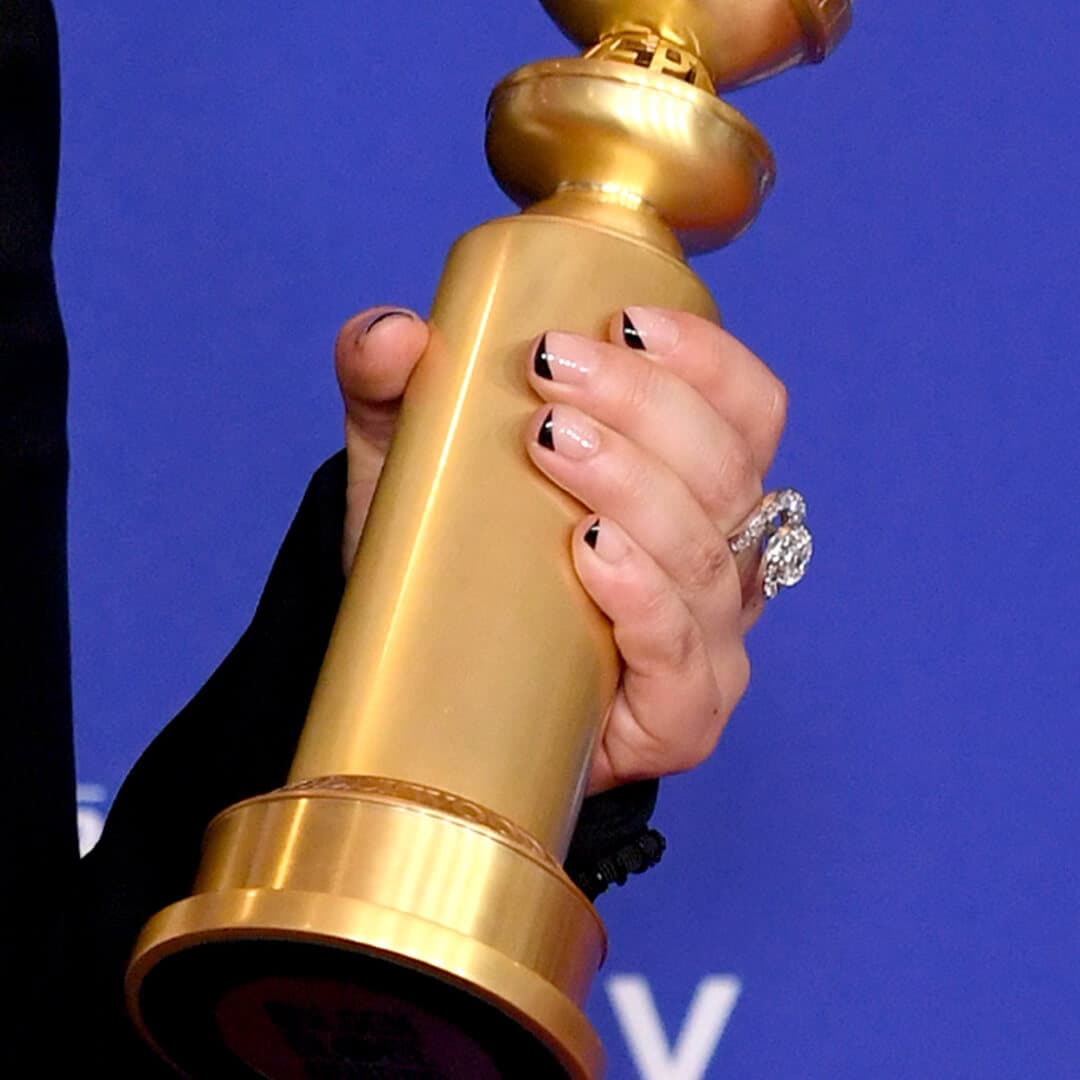 Close up of Awkwafina's hand with black French moon nail art holding a Golden Globes Award statuette