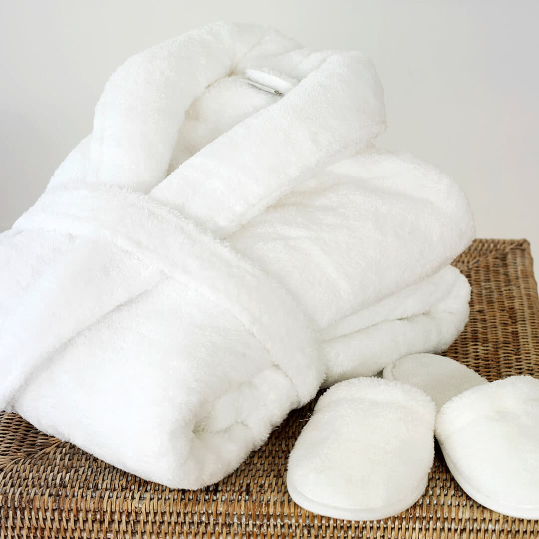 Fluffy white bathrobe and bedroom slippers on woven box