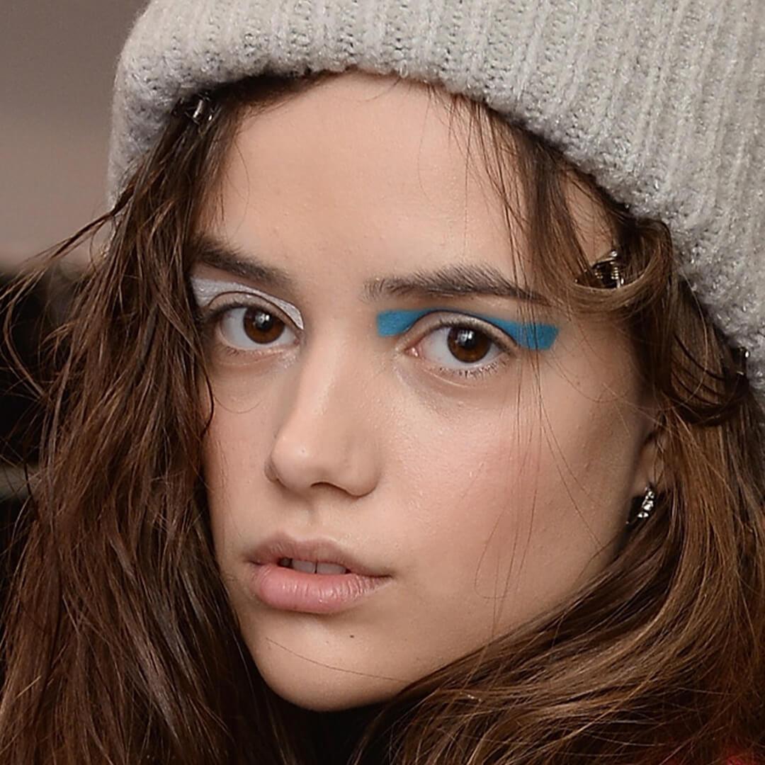 Close-up image of a model wearing a grey beanie rocking a multi-colored eyeshadow look