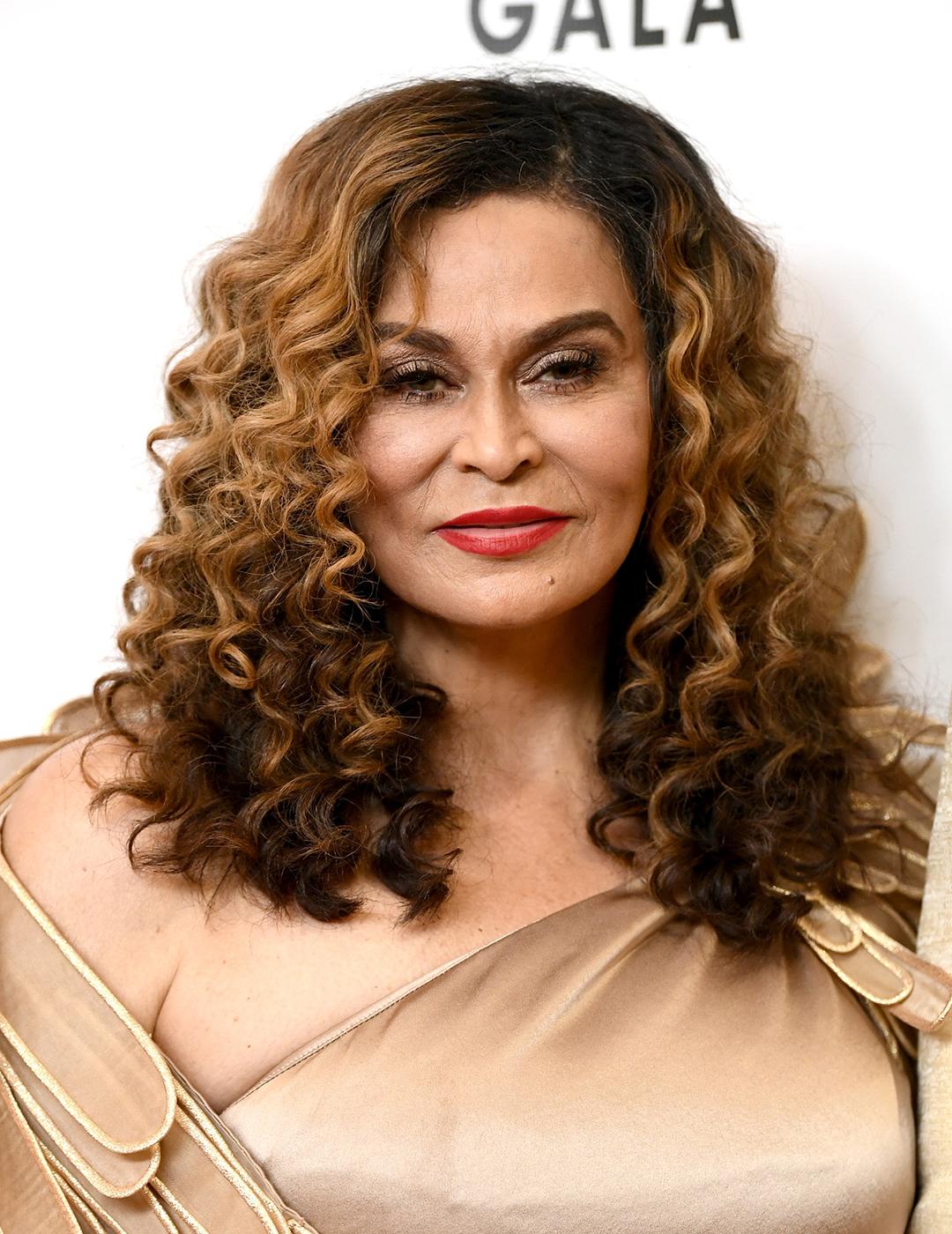 A photo of Tina Knowles in her honey-colored Mid-Length Coils dressed in a cream colored dress with a feather like cape 