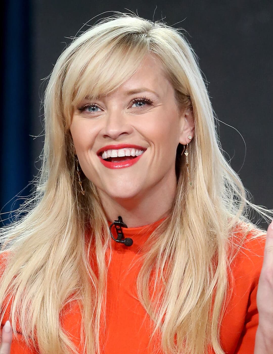 Smiling Reese Witherspoon rocking an orange dress and warm makeup look