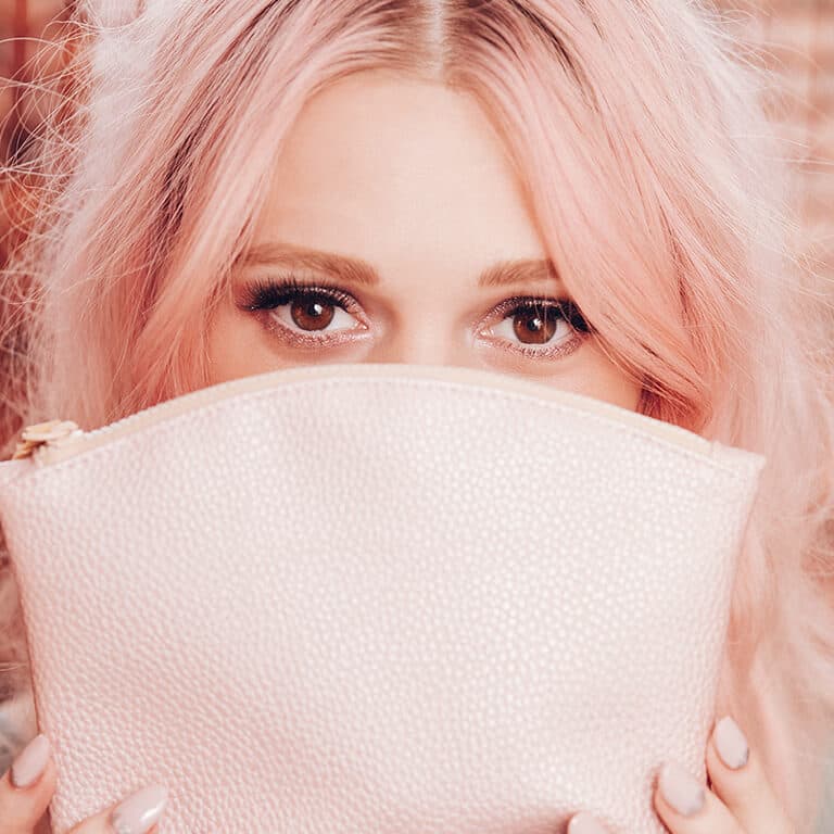 An image of a model covering half of her face using a soft pink makeup bag 