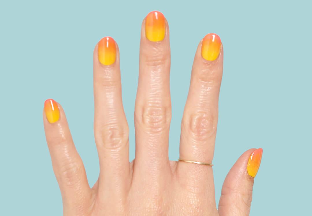 Close-up image of a hand with a yellow to orange ombré gradient nail art mani against a teal background