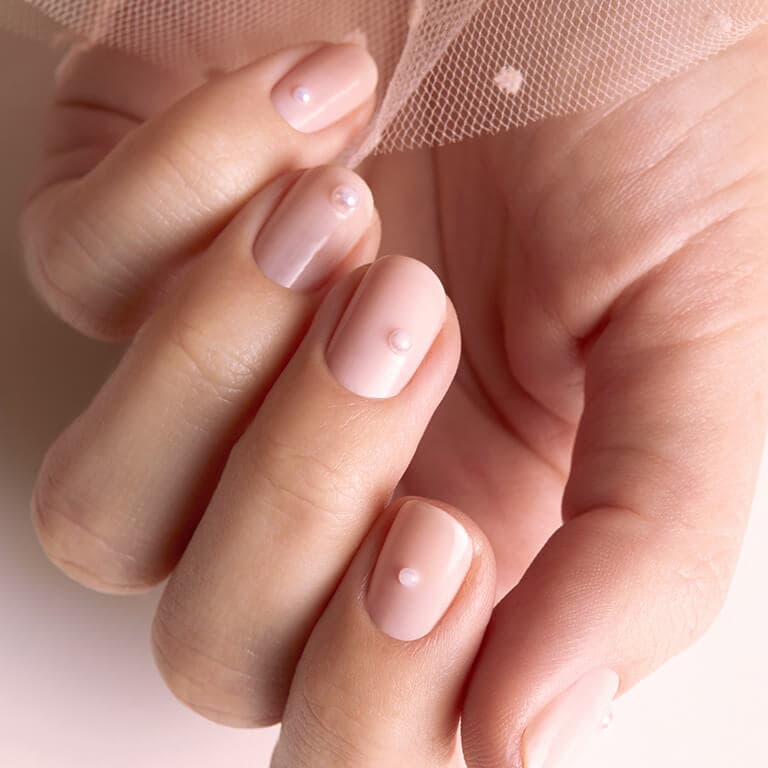An image of a model's hand with pearl accented mani holding nude pink tulle
