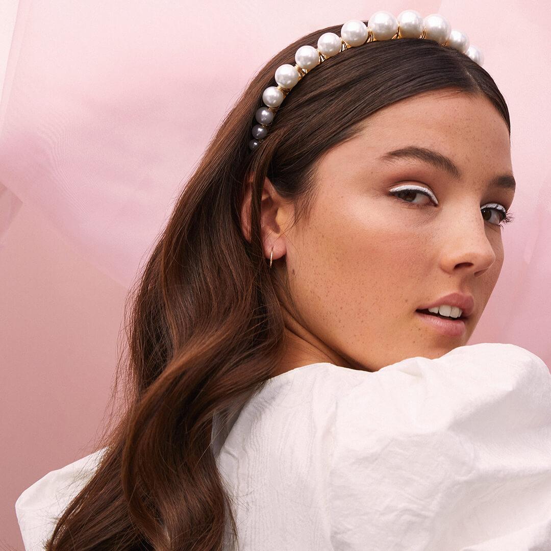 Close-up image of a model rocking a white eyeliner look and pearl-studded headband