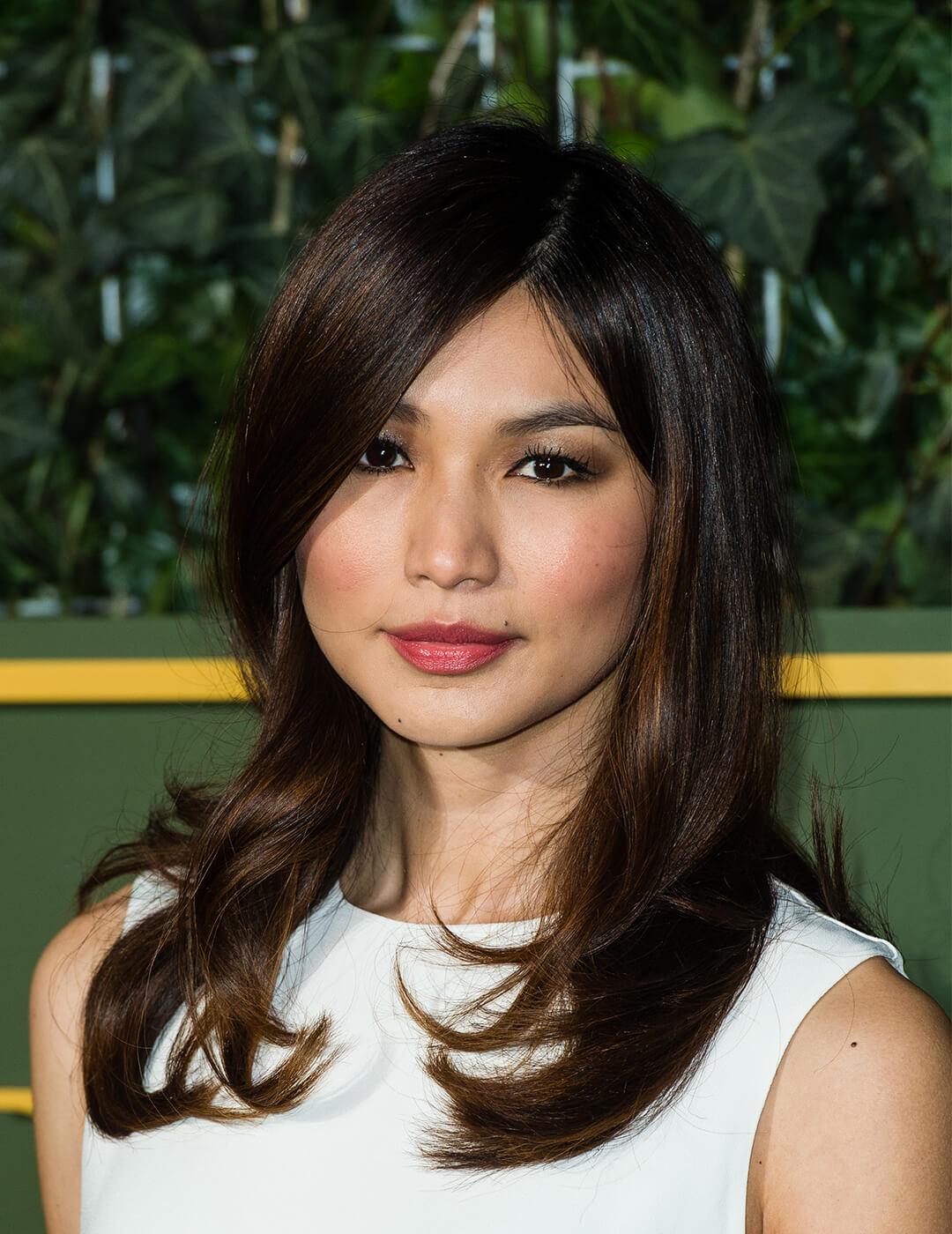 Close-up image of Gemma Chan rocking a neutral makeup look, white dress, and blowout hair