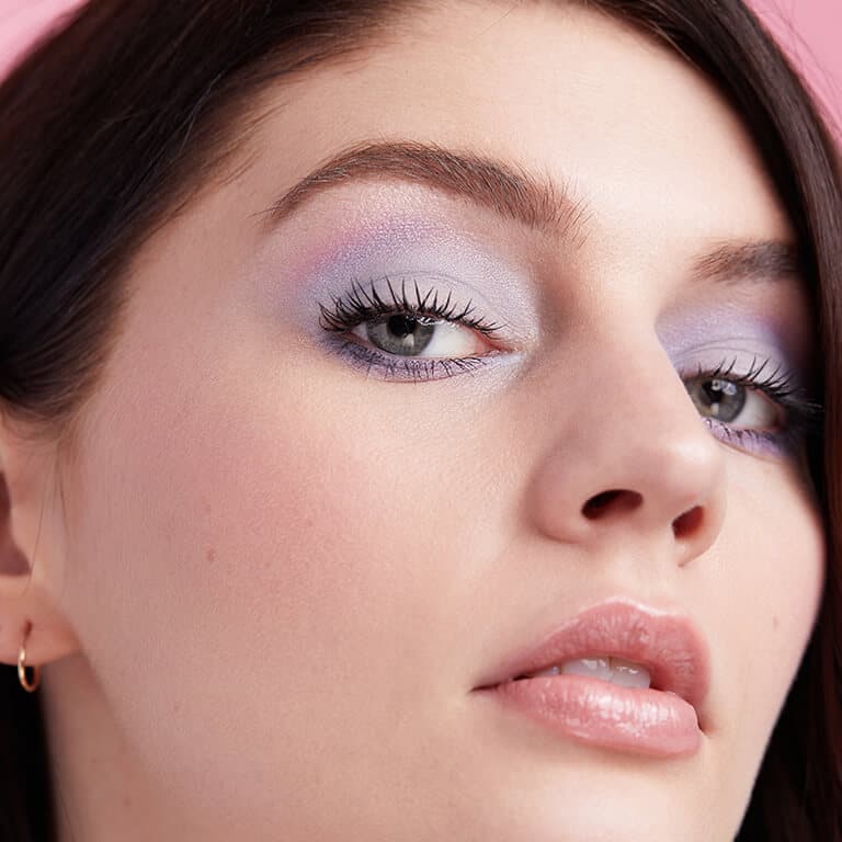 A close-up image of a model wearing a matte pastel blue and pink eyeshadow look paired with a nude pink lipstick