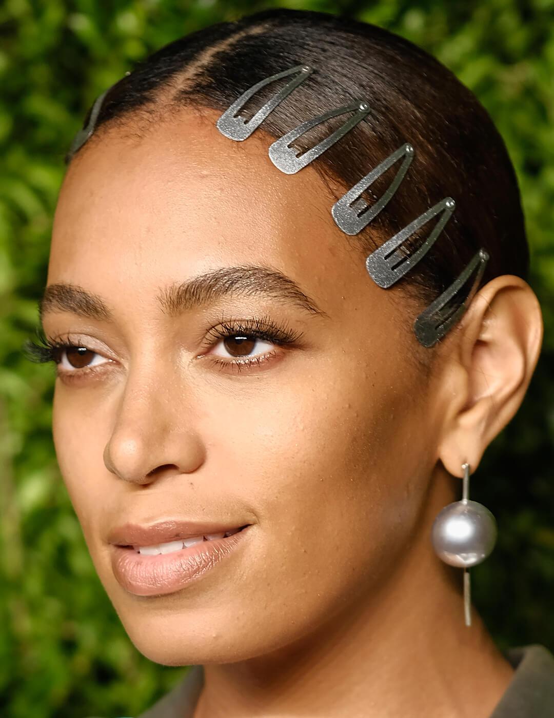 A closeup of Solange Knowles wearing a silk blouse with five dark green hairclips and a big pearl earring