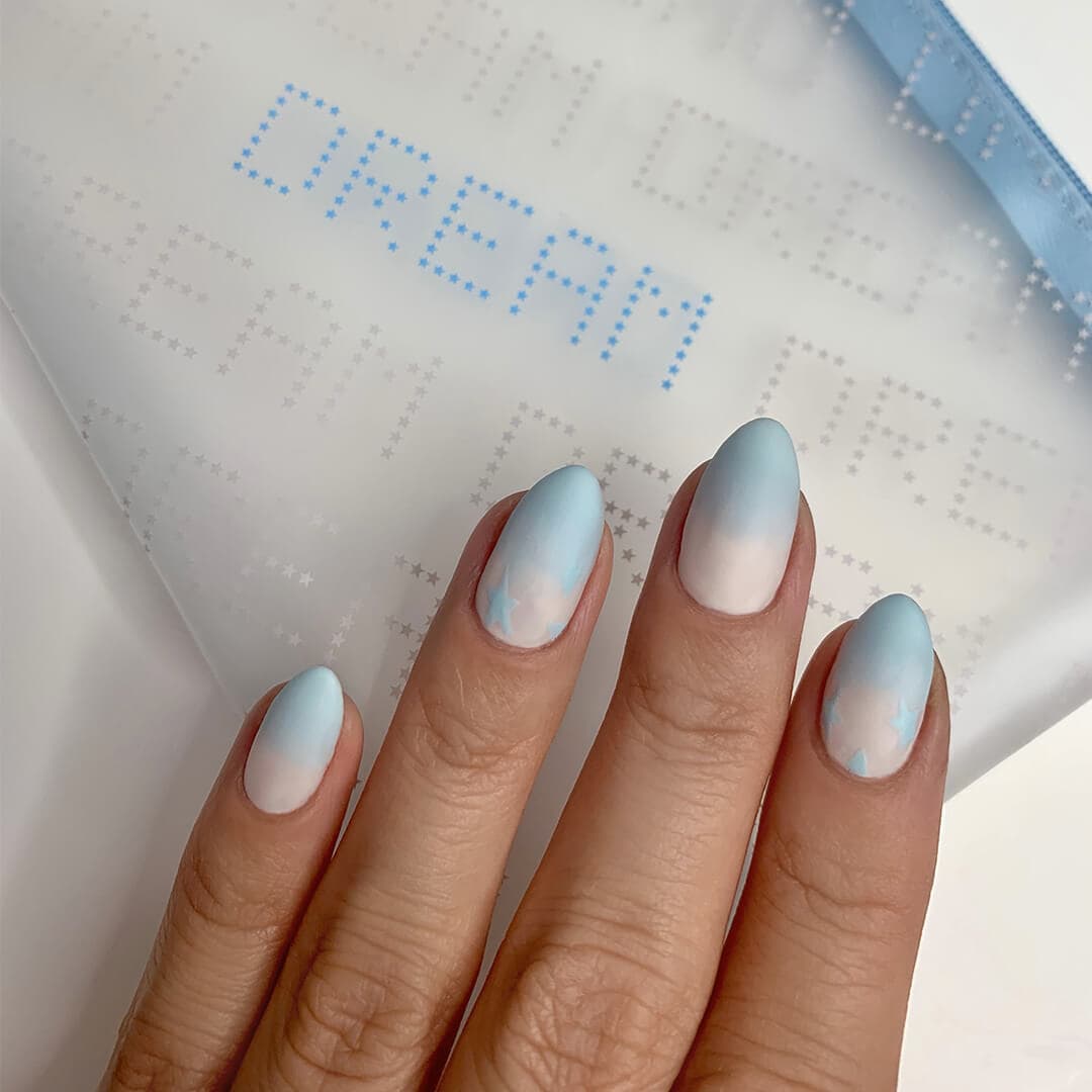 Close-up of woman's nails with white to blue ombre nail art mani on top of the IPSY January 2021 Glam Bag