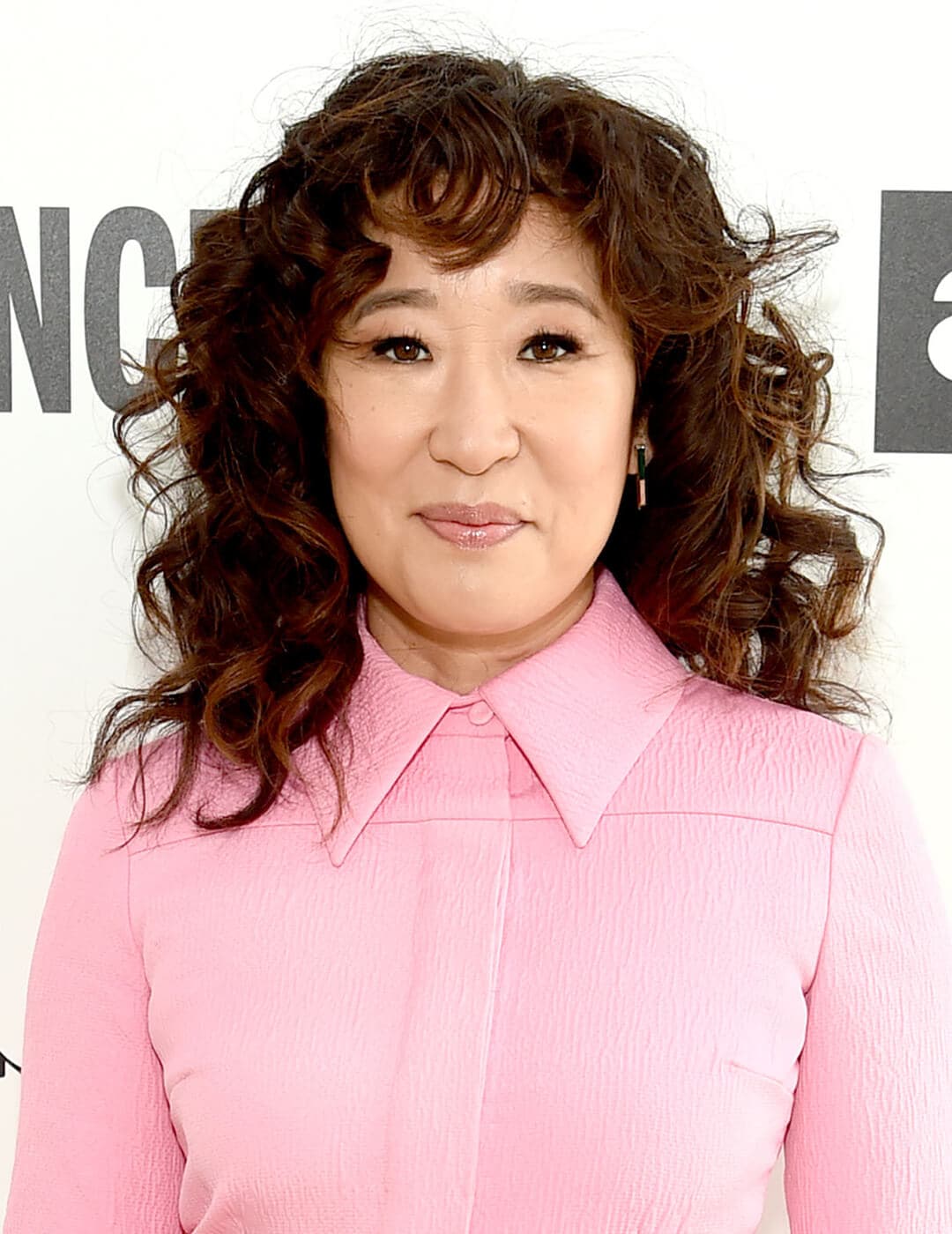 Smirking Sandra Oh rocking a wavy hairstyle and pink jumpsuit