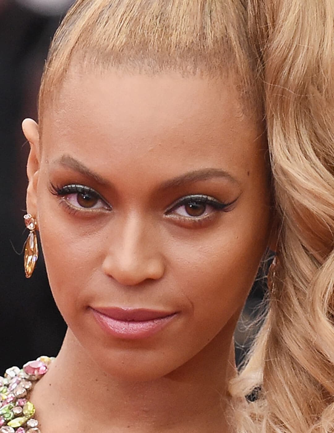 Beyonce looking glam in a high ponytail hairstyle, natural makeup look, and colorful stones dress