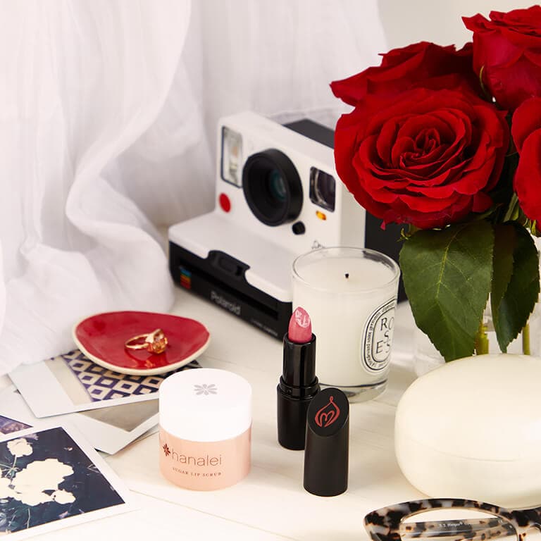 A image of lip products, candle, polaroid camera, roses, and a ring in a saucer