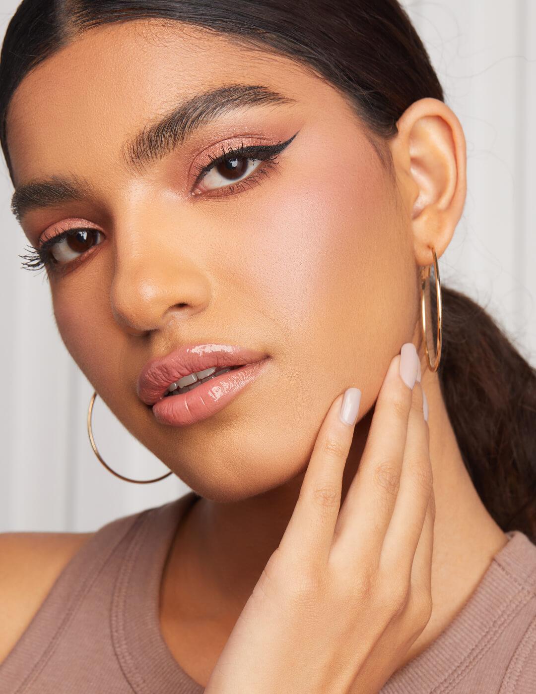 Close-up of a model looking chic with a rose gold eyeshadow and nude pink lips makeup look, and gold hoop earrings