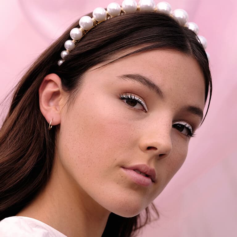 An image of a model wearing a white eyeliner look and a pearl-embellished headband