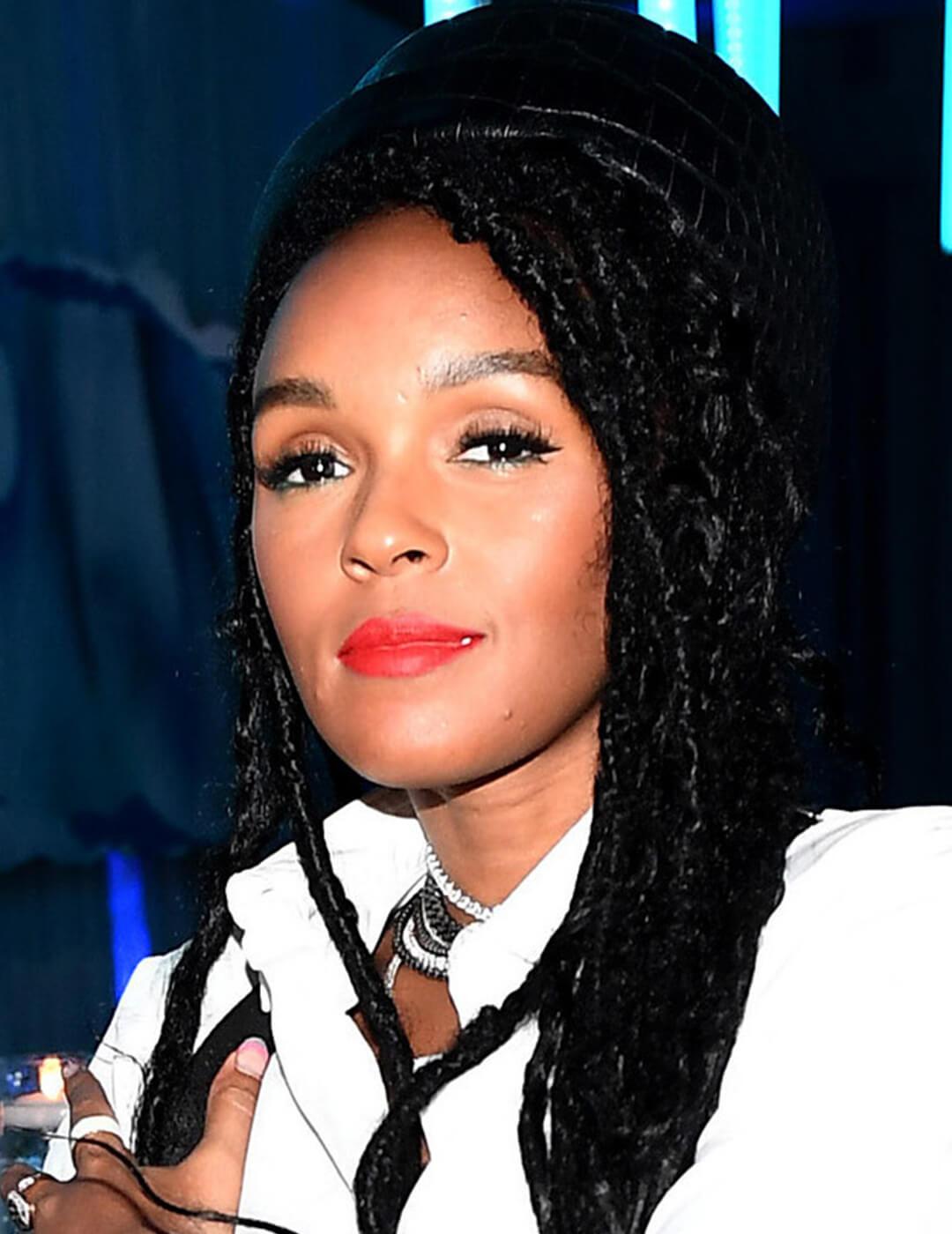 Janelle Monae rocking braided hairstyle, bold red lips makeup look, and black hat