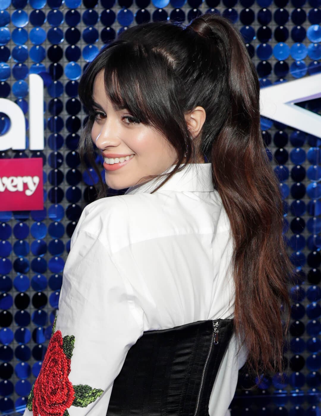 Camila Cabello rocking a white shirt with a rose print, black corsette, and high ponytail with bangs hairstyle