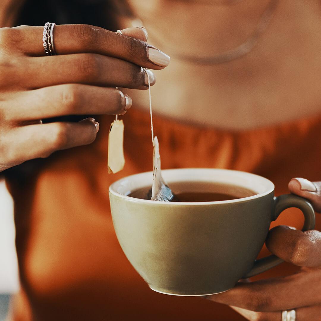 A closeup photo of a woman holding a cup of tea with teabag