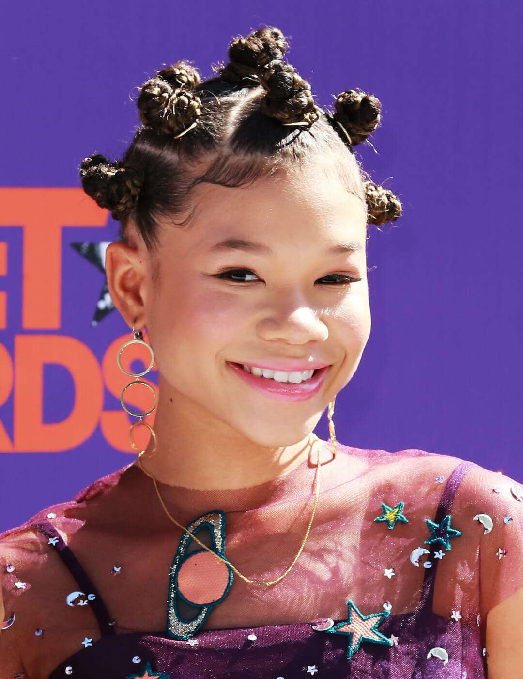 Close-up of a smiling Storm Reid looking cute in a outer space themed dress and bantu knots hairstyle