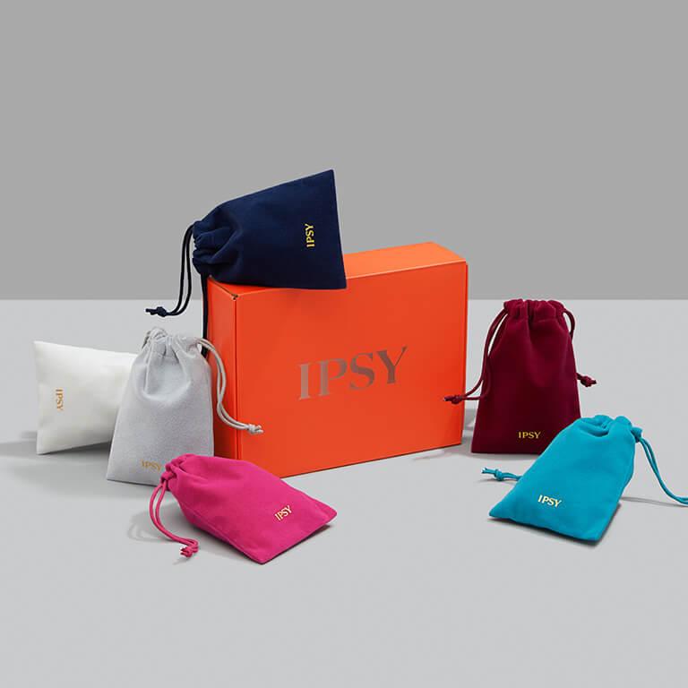 An orange box surrounded by different colored drawstring pouches all with gold IPSY logos