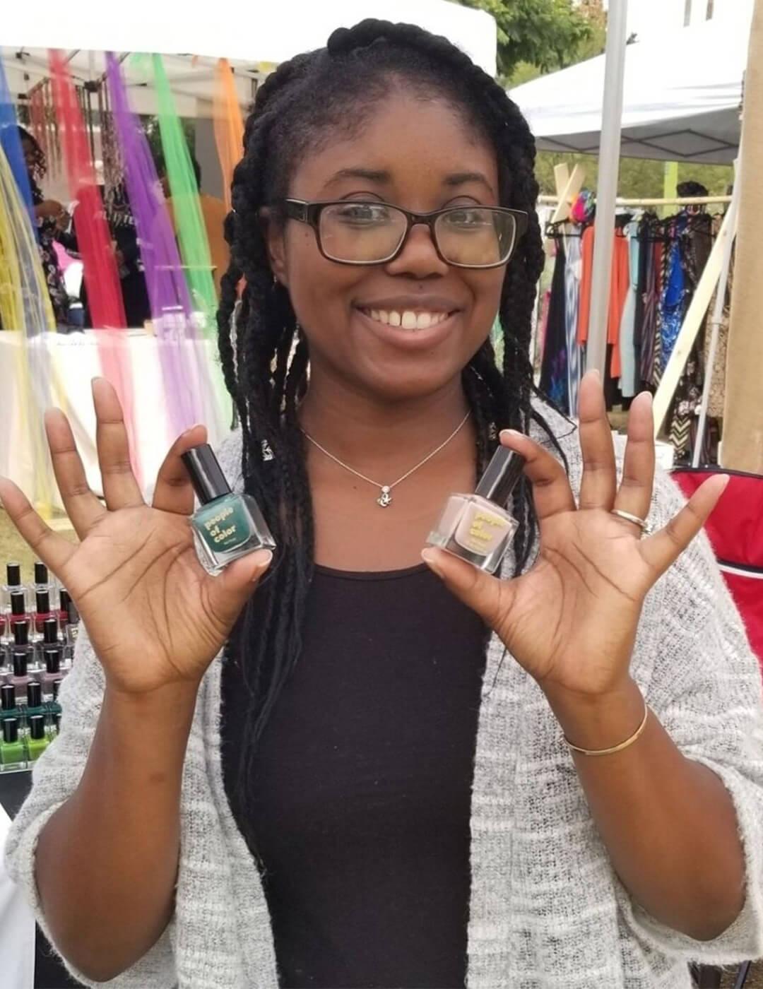PEOPLE OF COLOR BEAUTY founder Jacqueline Carrington posing and holding two bottles of nail polish