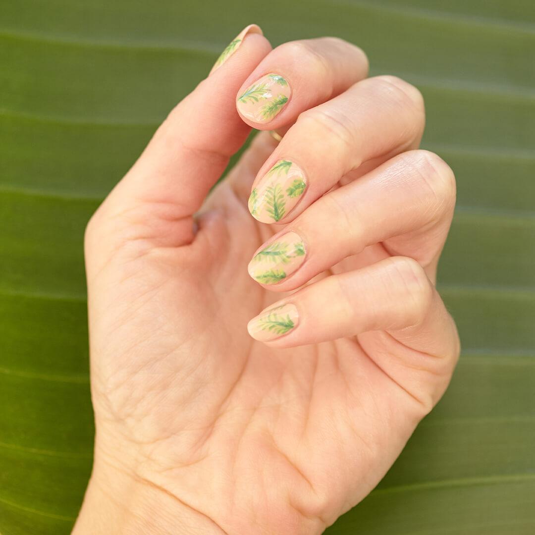 Close-up image of a hand with palm tree fronds nail art mani on a banana leaf background