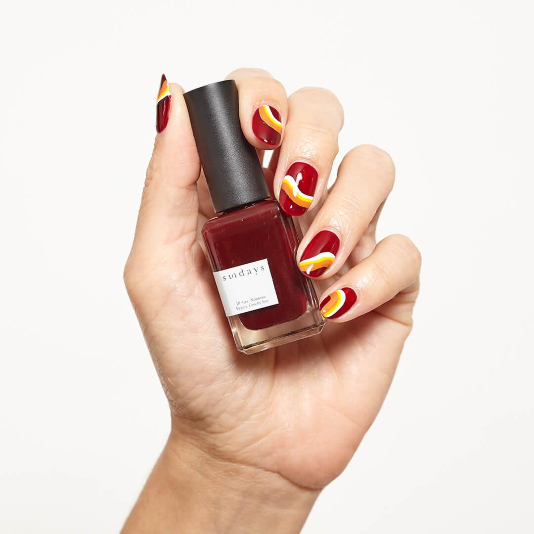 Image of a model's hand with colorful nail art holding the SUNDAYS Nail Polish in No. 18