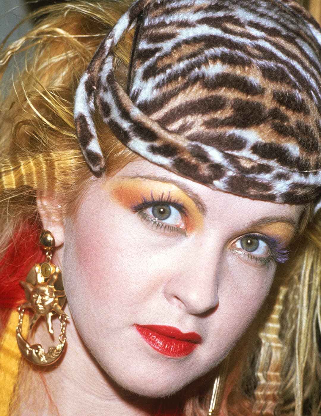 A photo of Cyndi Lauper wearing a leopard print hat and a colorful mascara look